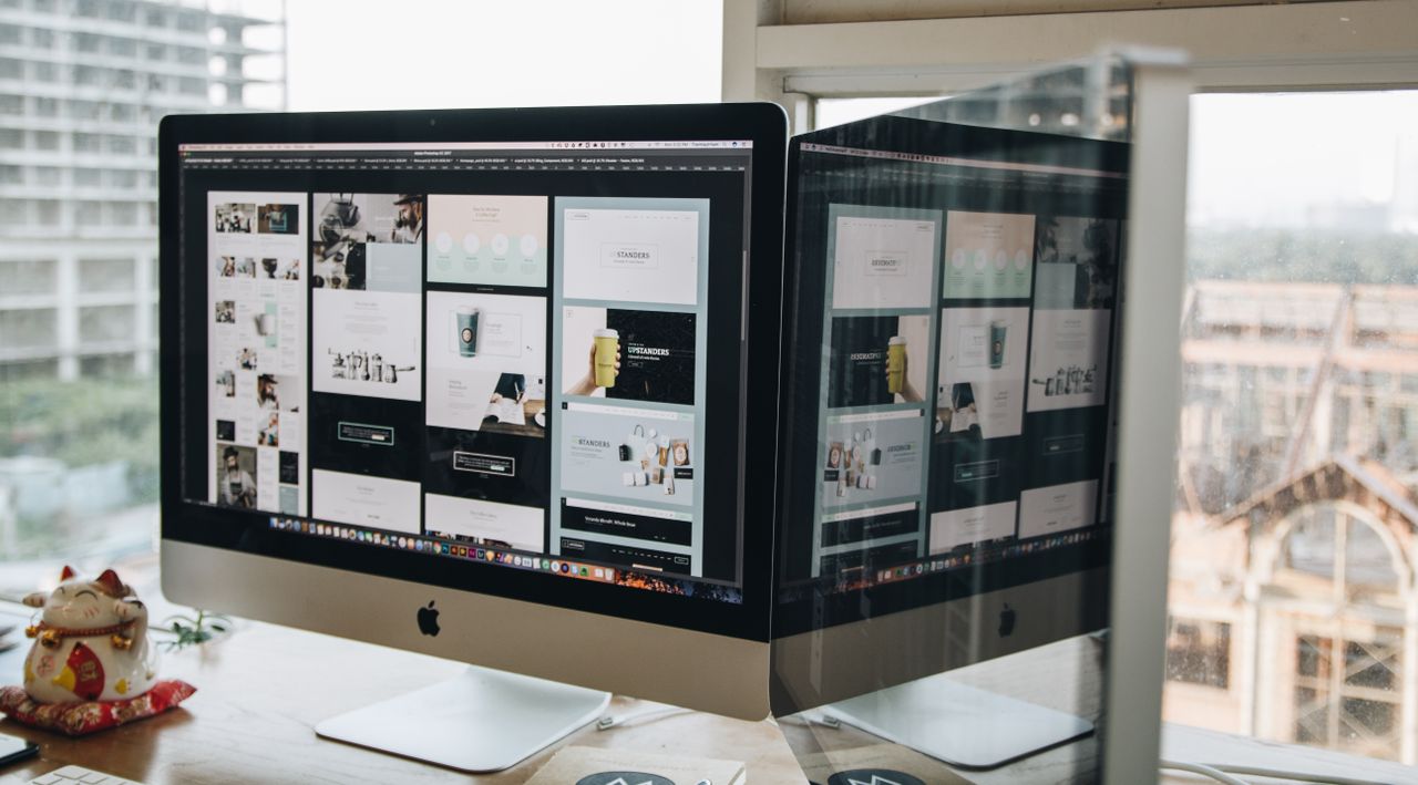 services-01 Two monitors on a desk display web design in a contemporary office environment.